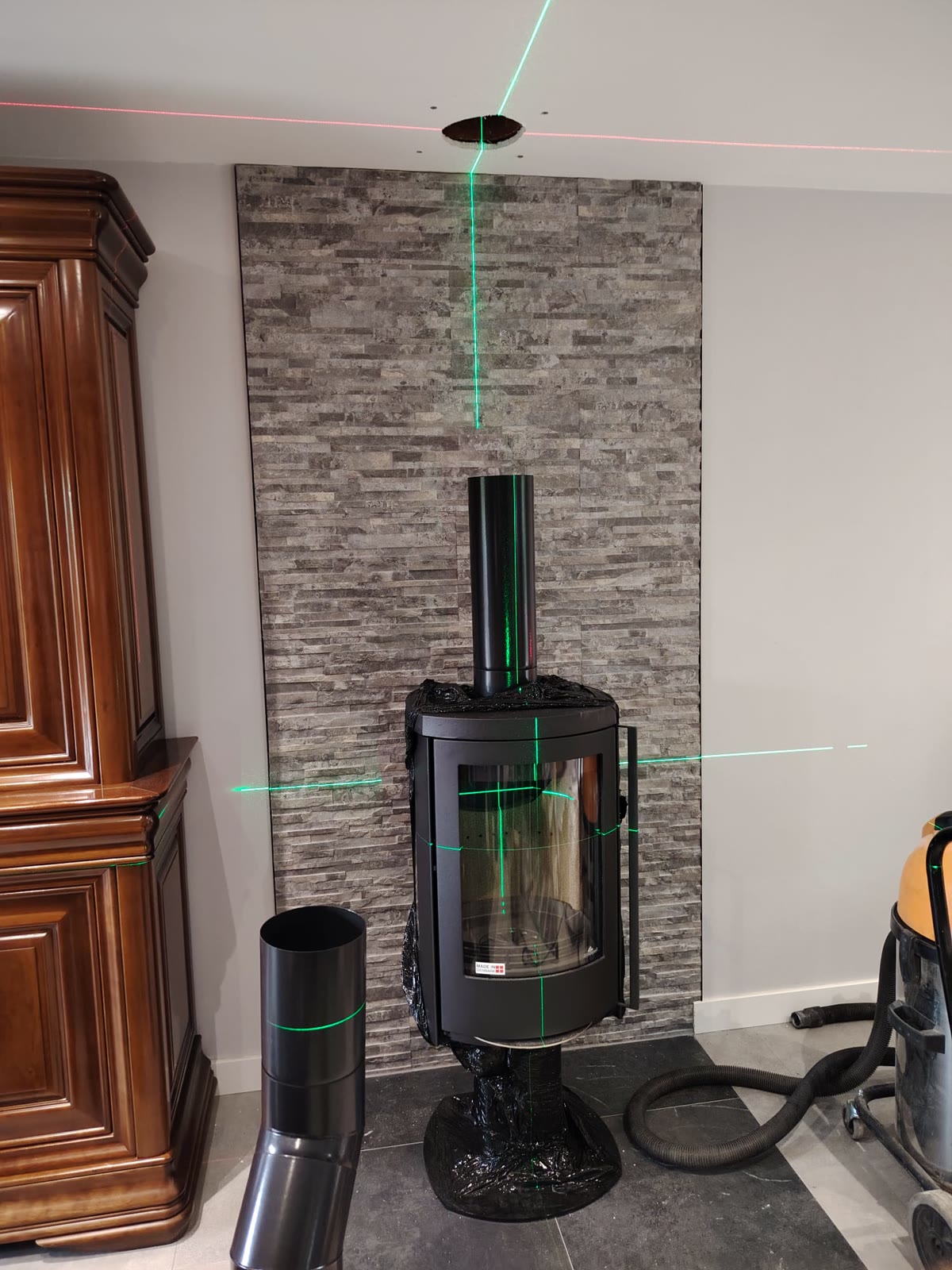 Poêle à bois sur pied aligné au laser devant un mur en pierre